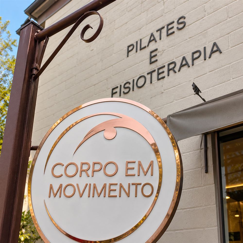 Placa redonda do estúdio Corpo em Movimento na entrada, com as palavras Pilates e Fisioterapia na parede ao fundo