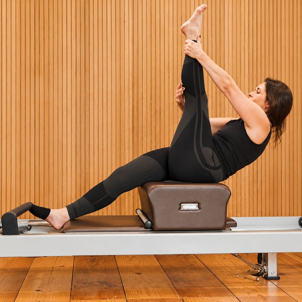 Exercício de Pilates no reformer, em frente a uma parede de ripas de madeira